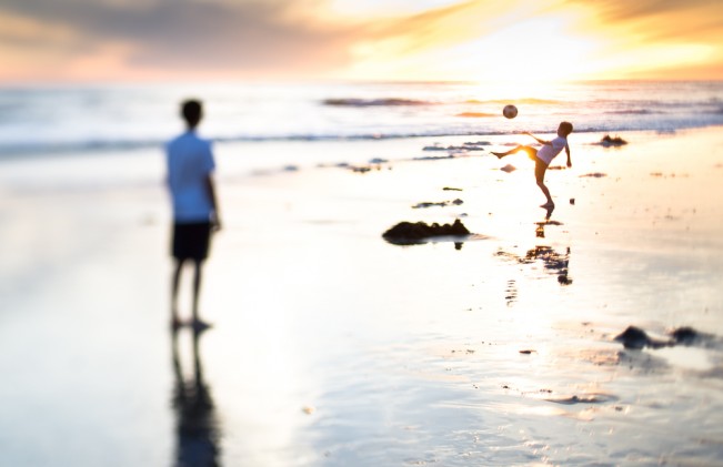 boys playing soccer on the beach