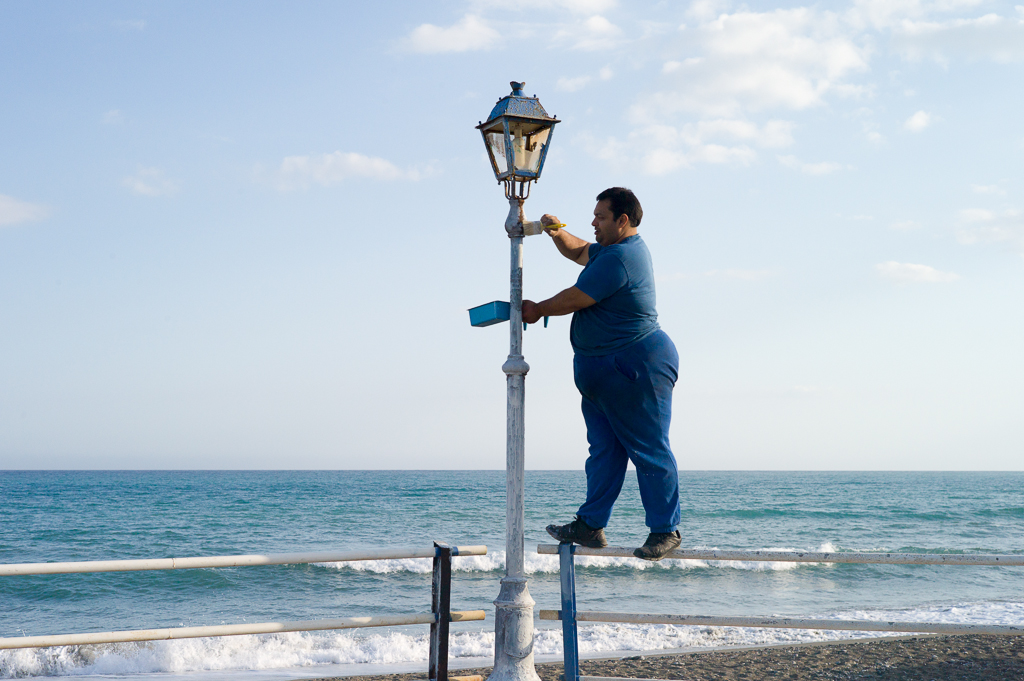 Ein Mann streicht eine Laterne am Meer an, Gra Lia, Kreta, Griechenland