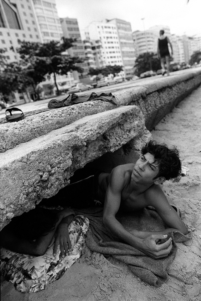 Teenage street kid sleeps in water runoff tunnel under side walk at Copacabana Beach, in the middle of the tourist zone.  2002