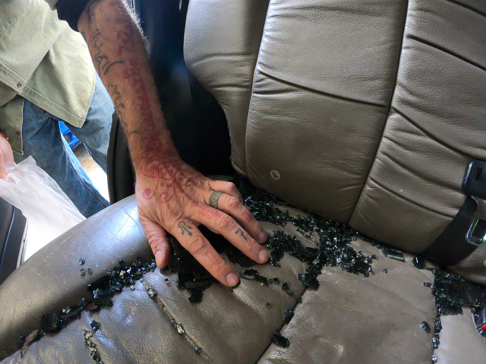 © Luis Alberto González Arenas, Inside the car where the camera was stolen, Wayne collects broken glass to use as an artifact for a new “Us & Them” camera.