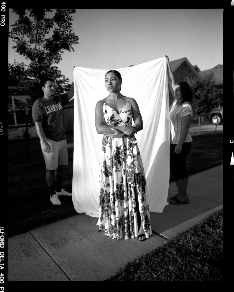 Elena Russey, 17, wears the dress she planned on wearing to prom before it was cancelled due to COVID-19 concerns as her mother and brother drapes a backdrop behind her on Wednesday, May 6, 2020 in Killeen, Tx. “I saw people laughing at the memes about our prom and graduation being cancelled and it really made me sad”. [Image produced on 120 film using a Pentax 6x7 Medium Format Film Camera]