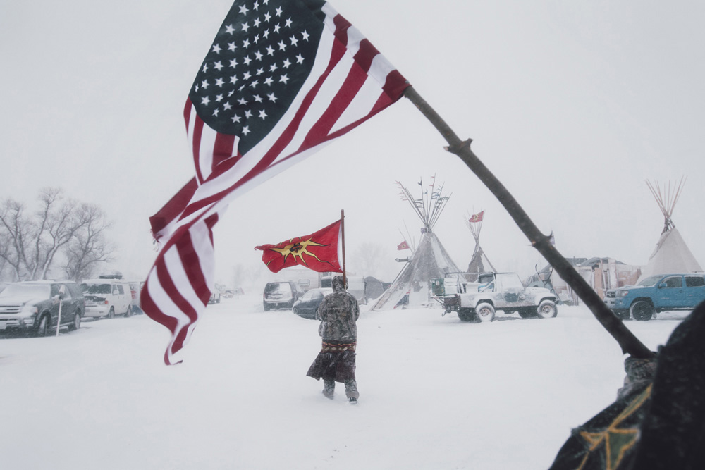 Two nations - Veterans carry an American and a Mohawk Warrior Society flag through the storm. The Mohawk flag came to prominence during the 1990 Canadian Oka Crisis, when the military confronted indigenous people in a major armed conflict for the first time in modern history. Camp is dedicated to stopping the Dakota Access Pipeline (DAPL) "in a good way" but there is some fear history will repeat itself, again.