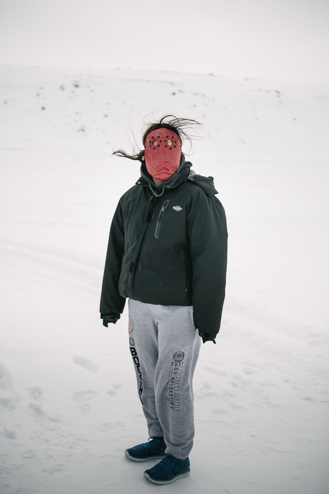 MB wears her mask of grief a few steps from family's front door. She lost her father to suicide last year, yet upon meeting in person, her resilience is evident in her energy and vibrance. April 12, 2018, Gambell, AK.