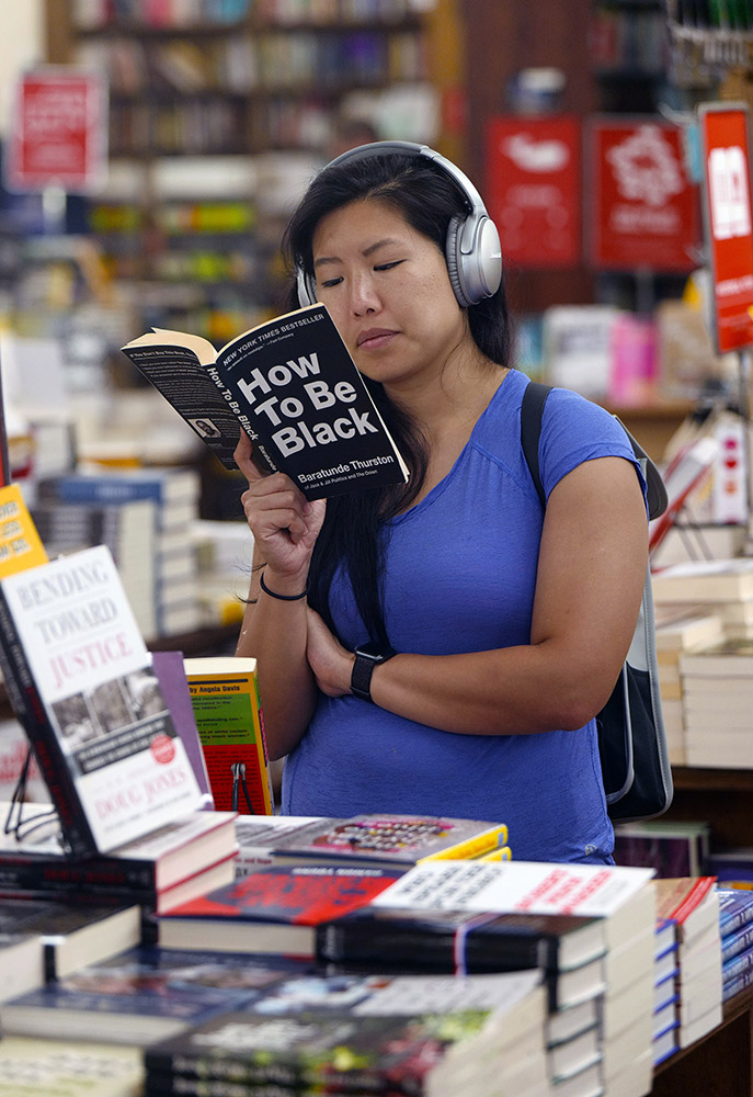 Reading Series—An Asian woman wearing headphones reads, HOW TO BE BLACK by Beratunde Thurston at the Strand Bookstore in NYC. first floor. Exclusive photo by Lawrence Schwartzwald