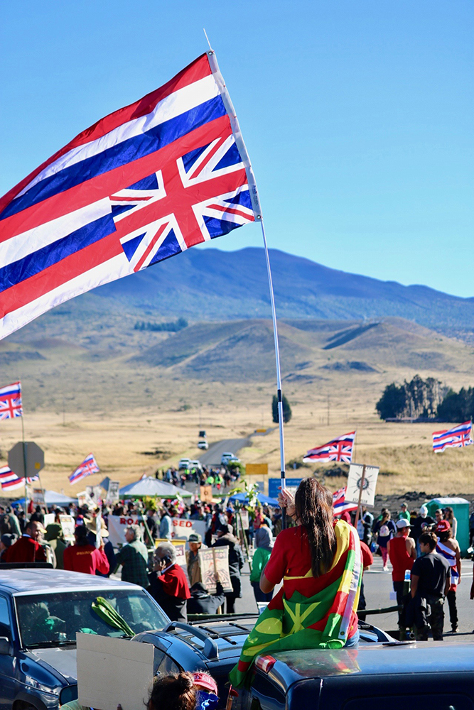 ©Kapulei Flores, Hold your hae high, July 2019. During the frontline stance in 2019 for the Protect Mauna Kea Movement, seeing the Hawaiian flag upside was a common thing. Historically our flag was flown upside down when our nation was in distress, so many of our people flew our flag upside down due to the mistreatment of our people and our land, including the proposed building of the TMT. Whether youʻre flying the flag upright or upside down, we always say to fly our hae (flag) high and proud no matter what.