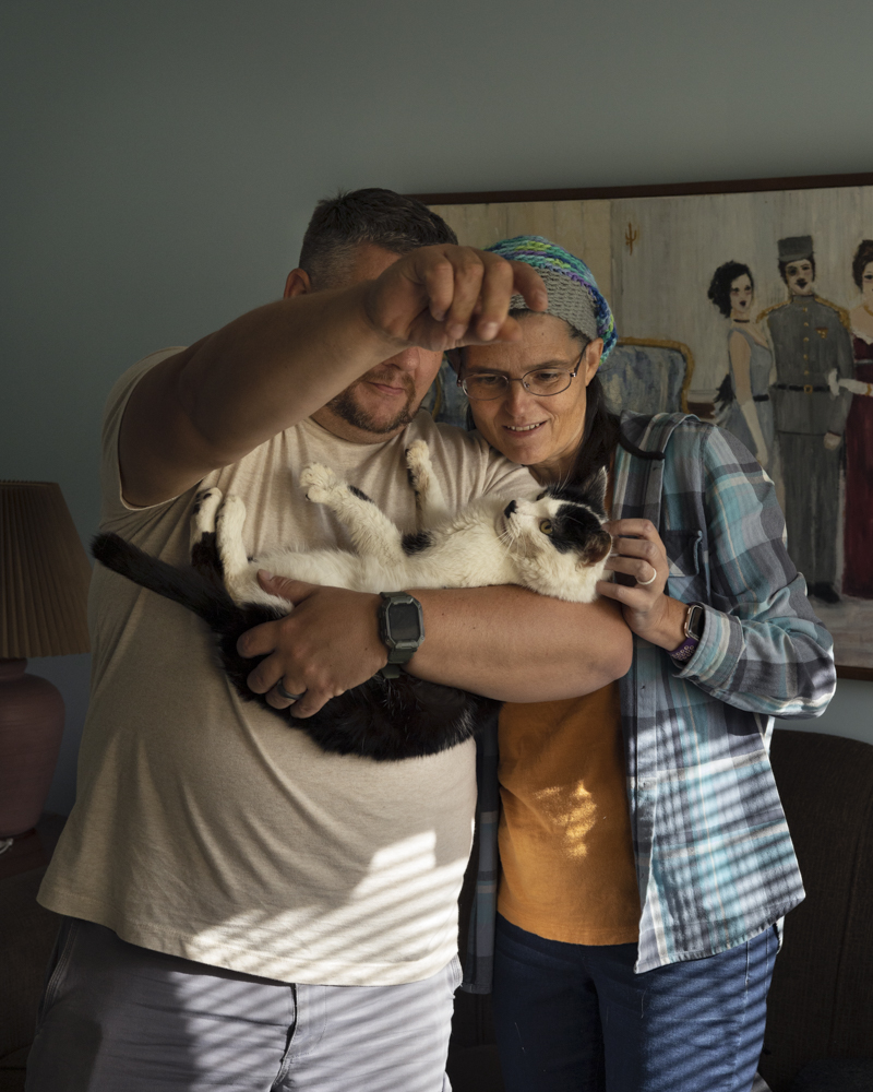 Christopher and Nancy Bukovsky stand in Nancy's mother's livingroom in Cherry Valley, NY and are cradling a cat named Edgar.