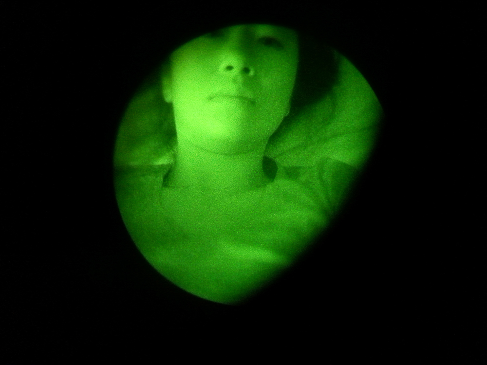Self-portrait through John Principe's night vision goggles in San Bernardino, California on October 4, 2012. With this device of war, I began to explore my domestic space and my role in this military structure.