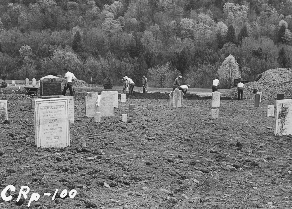 Disinterment of deceased from cemeteries and burying grounds in the reservoir area and reinterment at Pepacton Cemetery. Placing memorials and concrete markers at graves, and resurfacing the cemetery by placing topsoil, seed and fertilizer. Work done by Board's force. Camera located in roadway, 15' south of Section 43, looking Southeasterly. View shows the Board's force spreading material which was moved from the storage pile at upper right corner and dumped at Section 75 and 76. In the foreground is seen material which has been spread and graded, but not raked. The memorial to Dr. Peter W. Bouton and family, embedded in a concrete base (which has been covered) is seen in the left foreground.