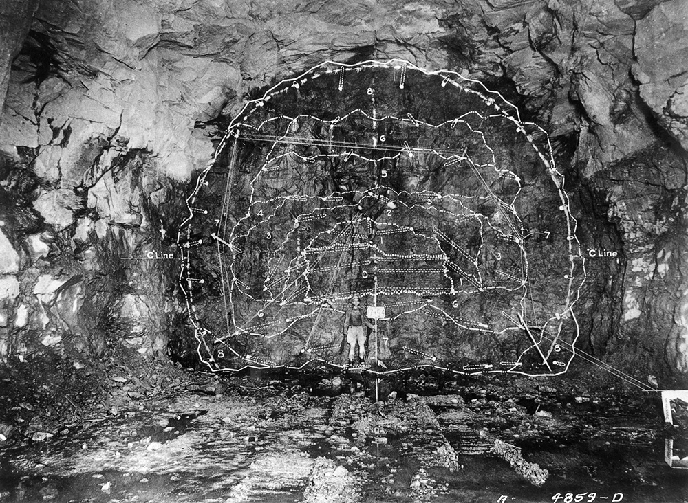 Neversink Reservoir. Neversink Dam. Neversink Division. Construction of coffer-dam and diversion tunnel and sinking of exploratory caissons. Contract 360. George M. Brewster and Son, Incorporated, contractor. Diversion tunnel south heading. Camera located on center line of diversion tunnel at Station 18+00 looking north. View showing heading, Station 17+54, with actual positioning and angling of its 68 drill holes. There were 6 cut holes 16 feet deep and 62 14-foot holes comprising first and second relievers, breakdown, lifters and line holes. Heading as loaded: 68 primers 1.25 inches by 8 inches at .40 pound, 40 percent gelatin; 1,240 plain sticks 1.5 inches by 8 inches at .56 pound, 40 percent gelatin. There are superimposed upon the photograph white lines diagrammatic of the break areas for the numbered delays. Drilling lies within the "C line" for full faced horseshoe shaped section averaging 26 yards to the foot, the bottom being 10+/- feet above finished invert. February 27, 1942.