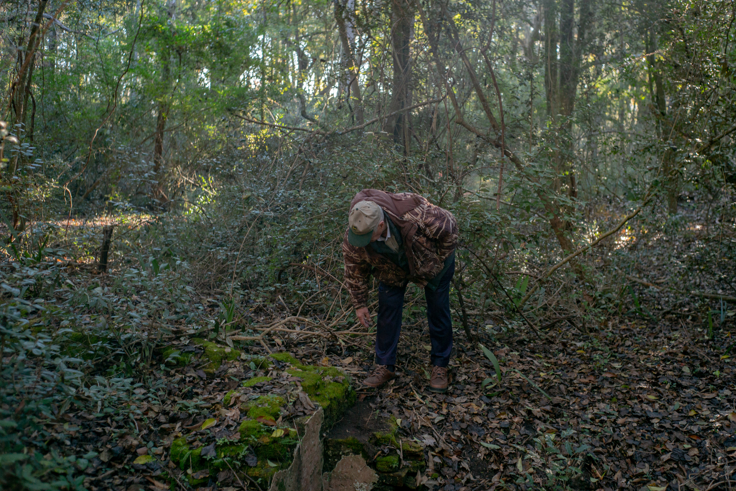 Jimmy Kerr bends down to look at a piece of the historic indigo vat ruins on his property, in Johns Island, South Carolina. Kerr played in the vat in the woods as a child, not realizing what it was.