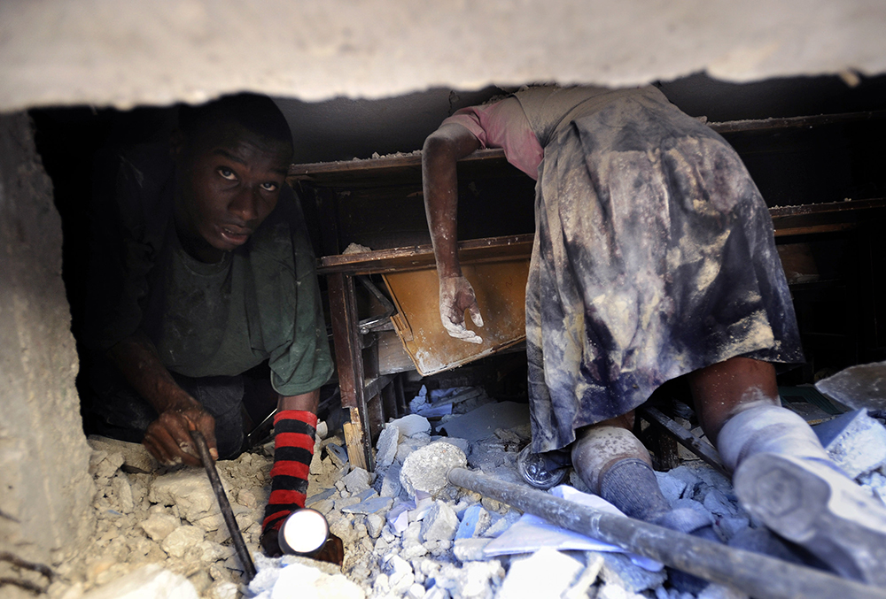 A Haitian man tries to rescue a live teacher trapped amid the rubble of the devastating earthquake in Port-au-Prince as he crawls past a schoolgirl that perished at Ecole St. Gerard.