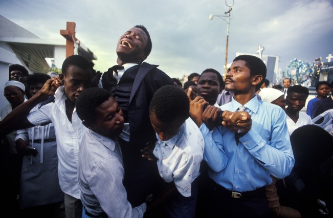 COPYRIGHT:  MAGGIE STEBER, PHOTOGRAPHER MOTHER'S FUNERAL--A young Haitian man writhes in grief at the funeral for his mother in the National Cemetery in Pt-au-Prince, Haiti in November 1987.  His friends and family lend support in his moments of anguish.  His mother was killed in pre-election violence in Haiti in the weeks leading up to the first presidential elections in 30 years, following the fall of the cruel Duvalier regime in 1986.  All-night shooting could be heard in Haitian cities during the weeks leading up to the elections. On election day, polls opened and closed within a hour because of widespread slaughter of voters and the burning of ballots and polling stations.