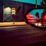 Color night street photograph framed through a car side mirror reflecting red lights and palm trees.