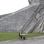 A souvenir seller waits for customers as she sits next to a monument to the WWII Battle of the Sutjeska, Tjentiste, Bosnia and Herzegovina, June 17, 2017. Thousands of monuments of all shapes and sizes were erected in Yugoslavia throughout the 1960's and 1970's to commemorate important historical events. A large number of the monuments were heavily damaged or destroyed on purpose in the 1990's conflicts. Those that survived are still visited by Yugoslavs and people who feel nostalgia for the old country.